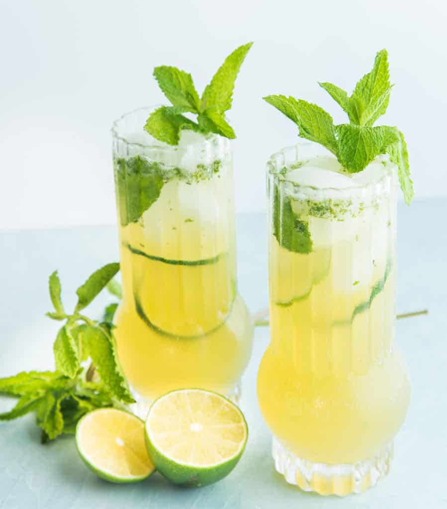 Two highball glasses filled with Puerto Rican style Mojitos and garnished with mint sprigs and lime wheels