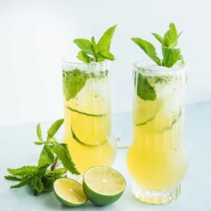 A horizontal image of Puerto Rican style Mojitos surrounded by cut limes and mint leaves.