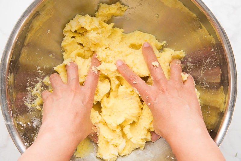 Hands mix the mashed potatoes in a metal bowl