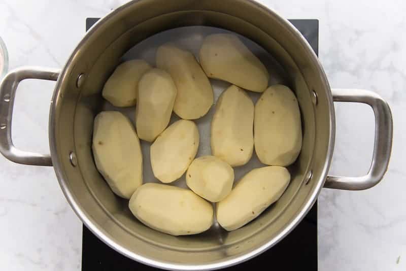 Whole russet potatoes are in a silver pot and covered with water