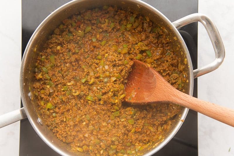 The finished beef picadillo is in a metal pan with a wooden spoon sticking out of it.