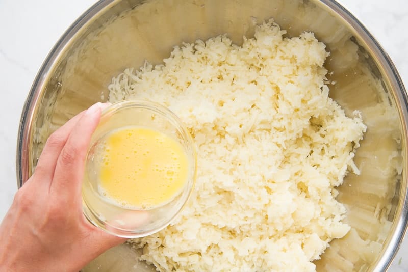 Beaten egg is added to the grated potatoes in a large metal bowl