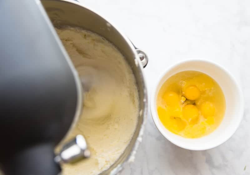 Eggs are added to the sugar and butter one at a time from a white bowl
