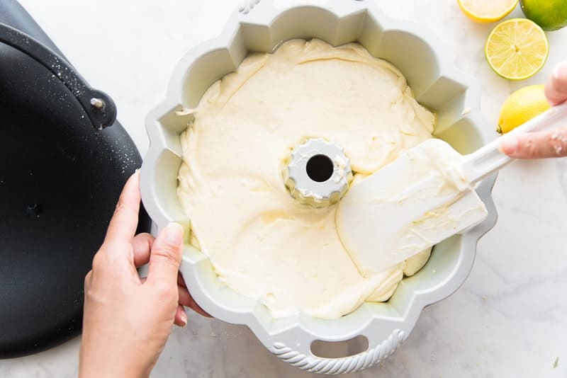 A hand smooths the poundcake batter in a cake pan using a rubber spatula