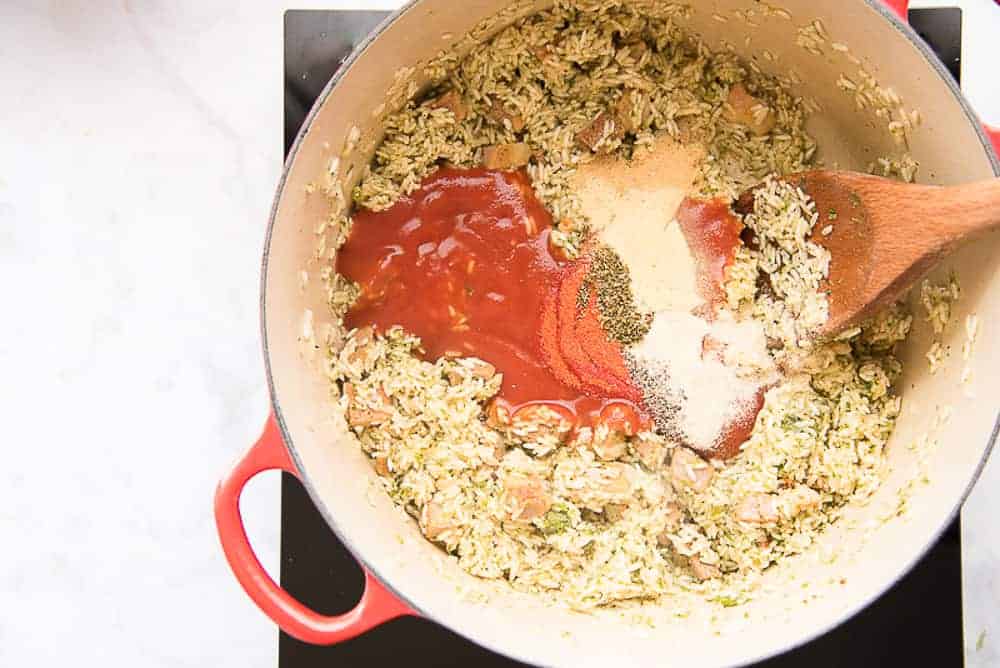 The tomato sauce and spices are stirred into the rice in the pot. 