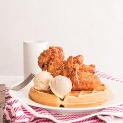 Chicken and Waffles with two scoops of Maple-Cinnamon Butter on a white plate over a red and white striped towel