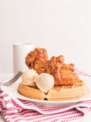 Chicken and Waffles with two scoops of Maple-Cinnamon Butter on a white plate over a red and white striped towel