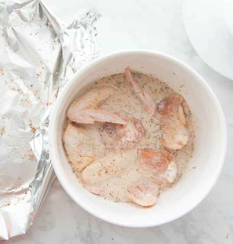 The chicken is soaked in a buttermilk marinade in a white bowl