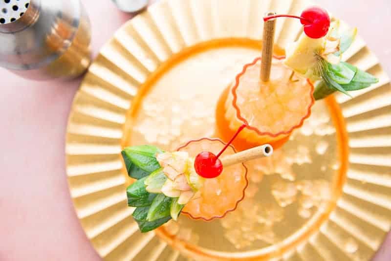Overhead image of a gold try with two Jungle Bird Rum Cocktails in highball glasses garnished with fruit birds