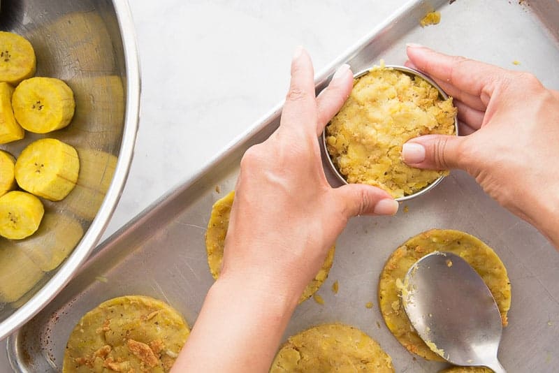 A hand presses the mofongo into a round form to create the burger "buns" on a silver tray.
