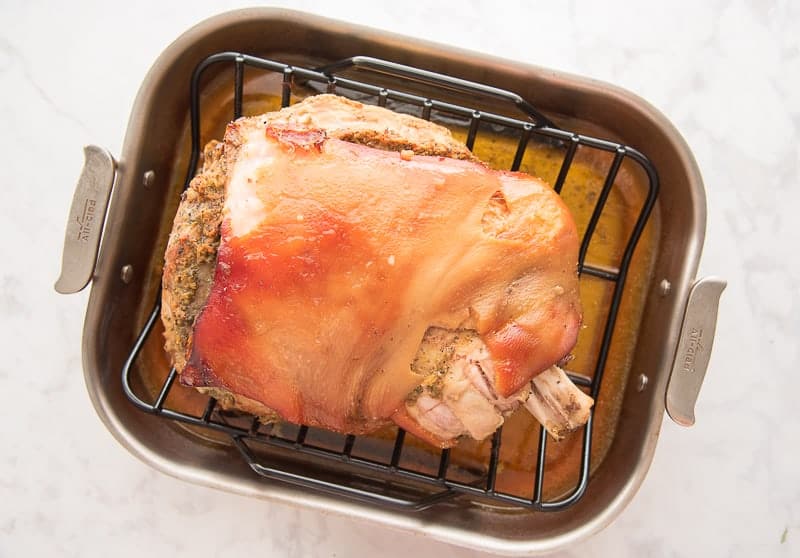 The partially cooked pernil is in a roasting pan.