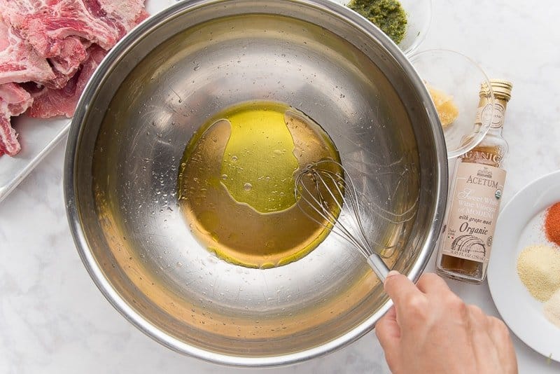 A hand uses a whisk to mix oil and vinegar in a silver mixing bowl.