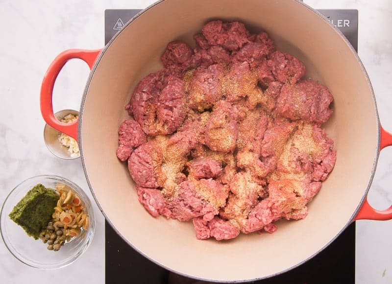 Ground turkey is seasoned with spices in a red pot