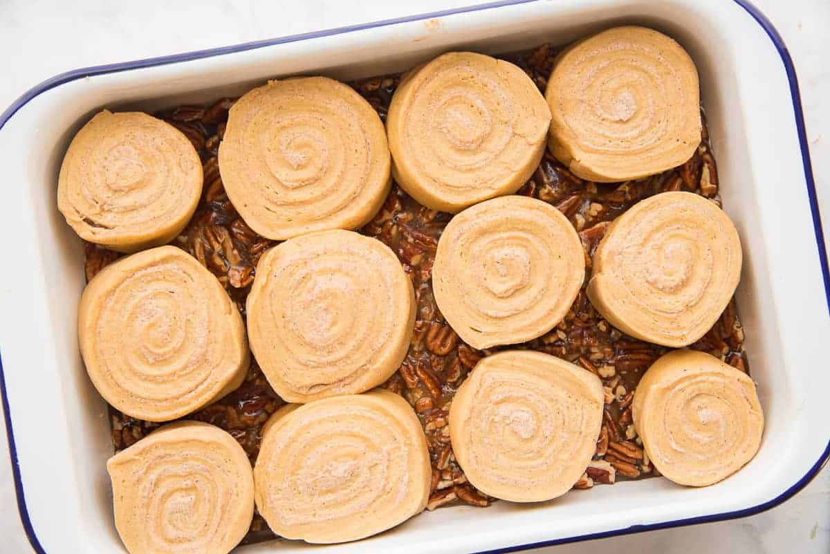 The pumpkin rolls are arranged in a white blue-rimmed pan that's been filled with caramel-pecan glaze.