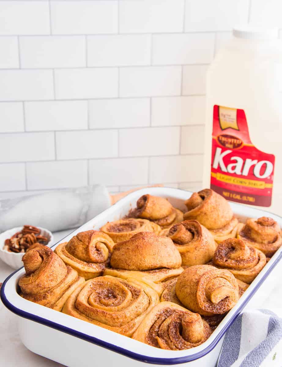 A white metal pan of baked Pumpkin Caramel Sticky buns in front of a large jug of Karo Syrup
