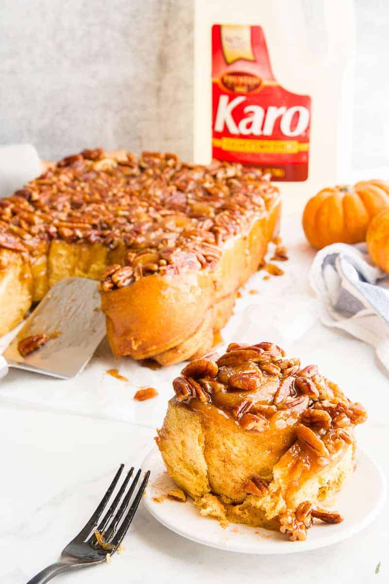 A Pumpkin Caramel Sticky Buns with a bite removed on a white plate. A bottle of Karo Syrup in right background.