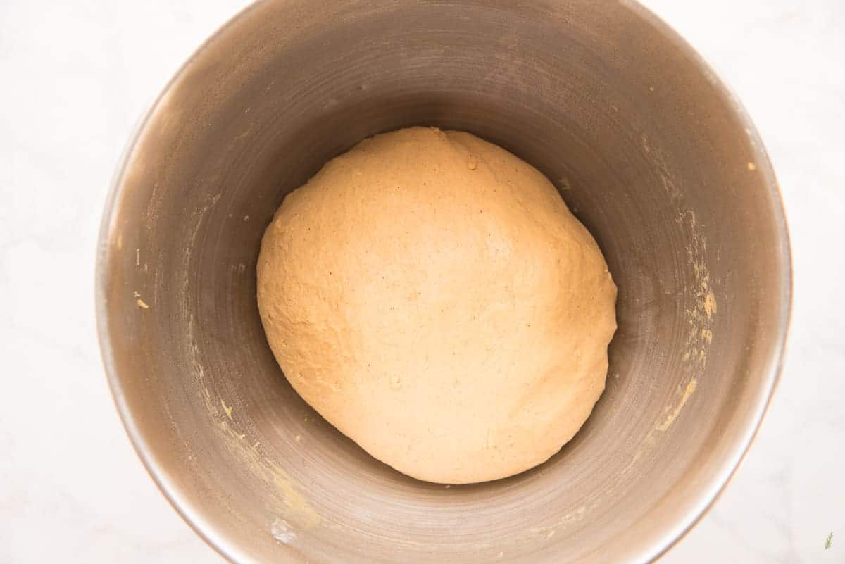 Light orange dough in a ball in a silver bowl.