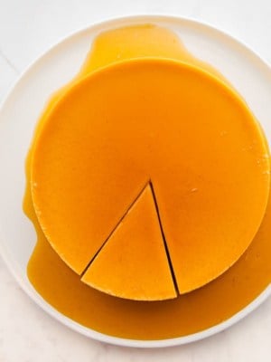 Orange whole flan with a piece cut on a white plate