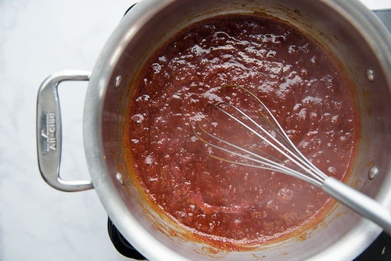 The curry sriracha sauce is thickened on the stove in a silver pot and stirred with a silver whisk