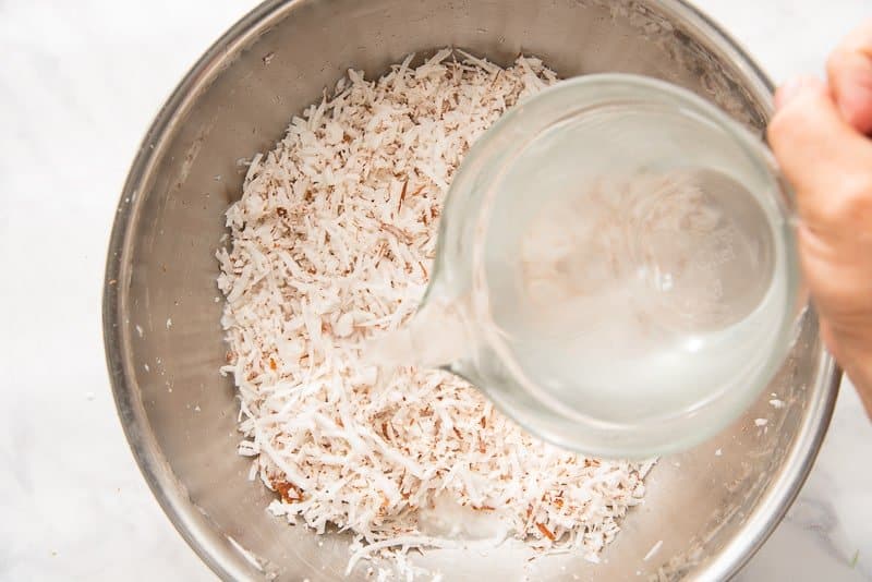 The soaking water is poured over the shredded coconut meat in a silver bowl