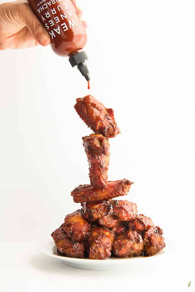 A hand squeezes a bottle of Curry Sriracha sauce over a stack of Curry Sriracha Air Fryer Wings