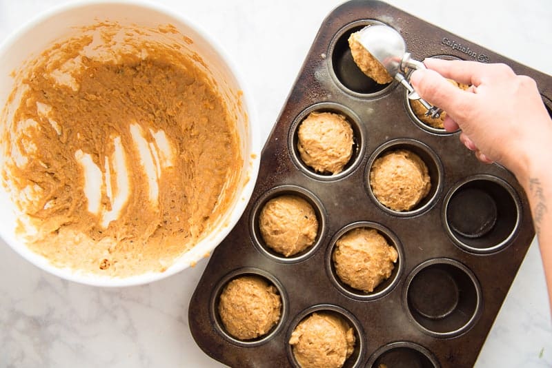 A hand scoops the muffin batter into a black muffin tin