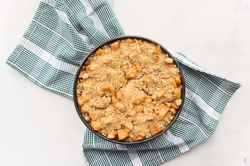 The baked Apple Streusel Cheesecake in a black pan on a green and white houndstooth towel
