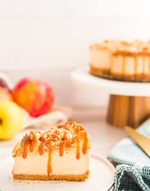 a portrait image of a slice of apple streusel cheesecake on a white plate.