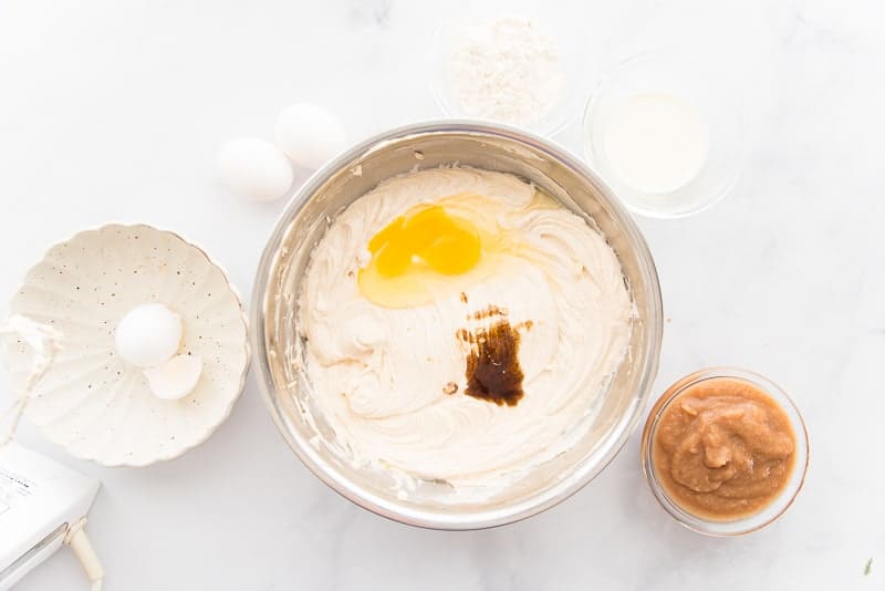 The eggs and vanilla are mixed into the cream cheese mixture in a silver mixing bowl