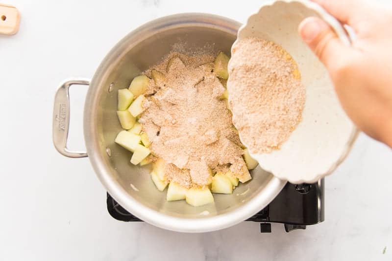 The cornstarch-sugar and spice mixture is added to the diced apples in a silver pot