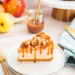 A horizontal image of a slice of Apple Streusel Cheesecake drizzled with caramel sauce on a white plate