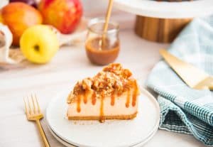 A horizontal image of a slice of Apple Streusel Cheesecake drizzled with caramel sauce on a white plate