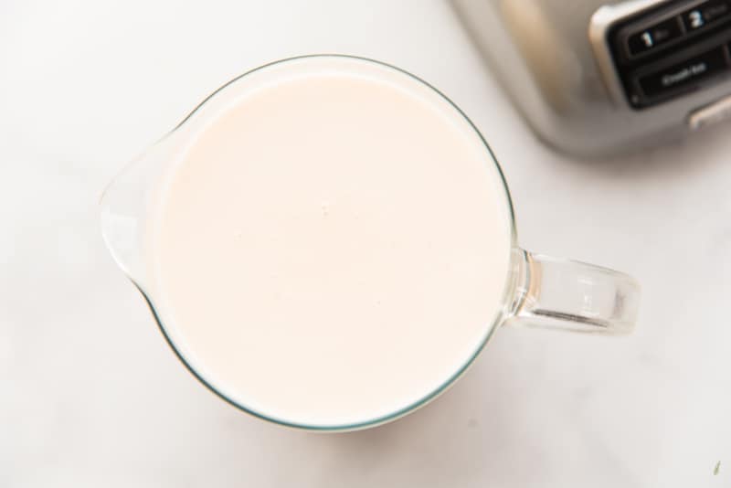 A clear, glass pitcher of coquito on a white background