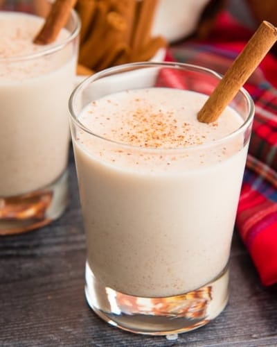 A glass of coquito garnished with a cinnamon stick next to a red plaid napkin