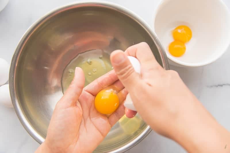 Hands separate egg whites from the yolks into a metal mixing bowl