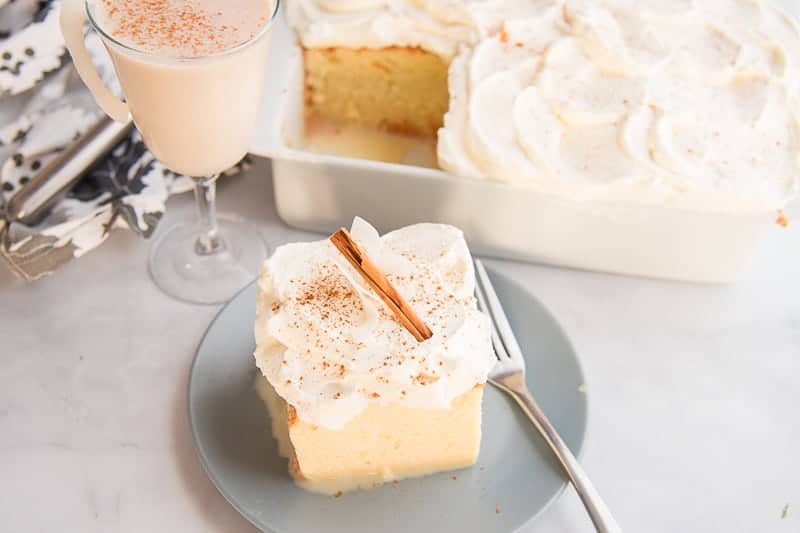 White frosting on a yellow coquito tres leches cake with a cinnamon stick on a grey plate