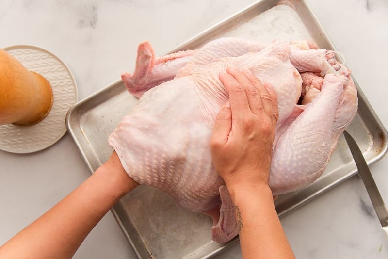 A hand separates the skin of the turkey from the flesh before seasoning it