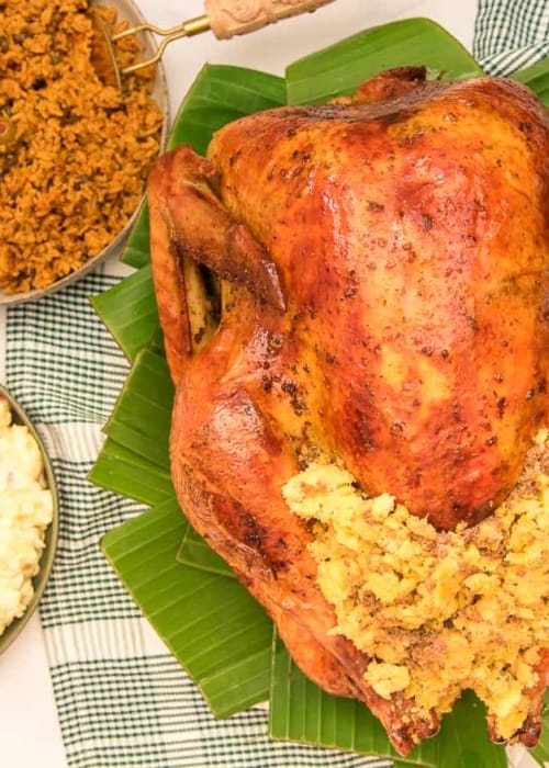 The Pavochon with Mofongo Stuffing on a bed of banana leaves next to bowls of potato salad and yellow rice