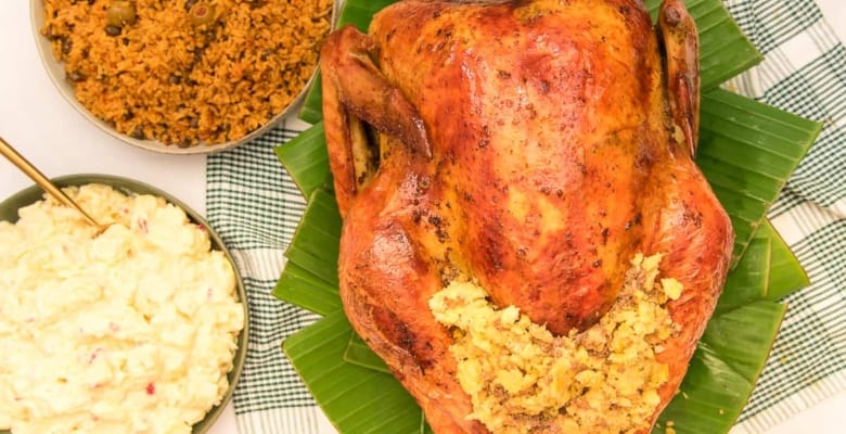 The Pavochon with Mofongo Stuffing on a bed of banana leaves next to bowls of potato salad and yellow rice