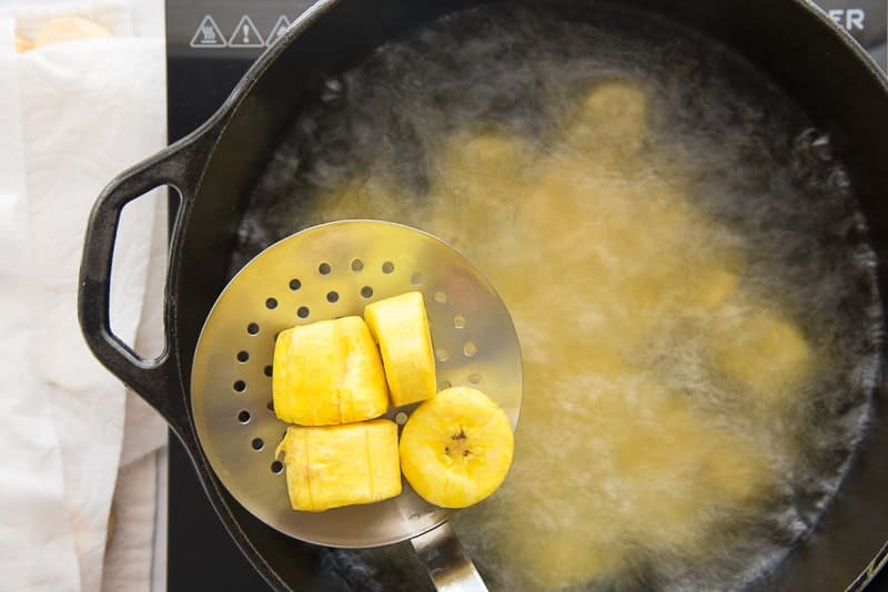 The fried plantains are removed from a black pot of oil