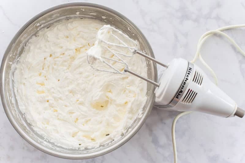 Whipped cream in a silver bowl. A mixer with silver beaters is next to the bowl
