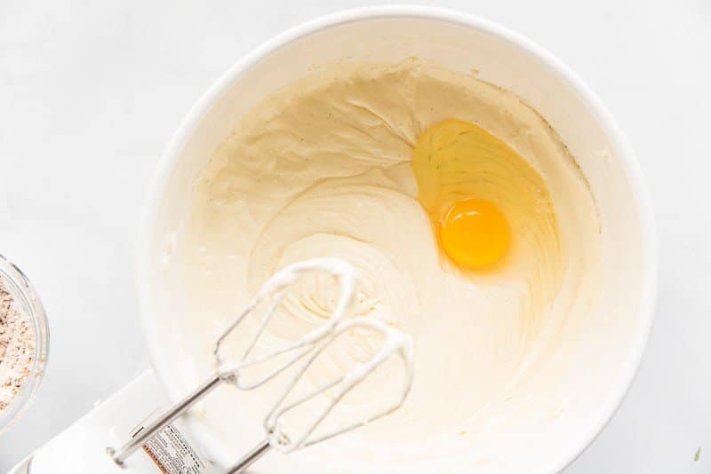 And egg is mixed into a white batter in a white mixing bowl