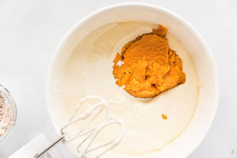 Pumpkin puree is added to white batter in a white mixing bowl