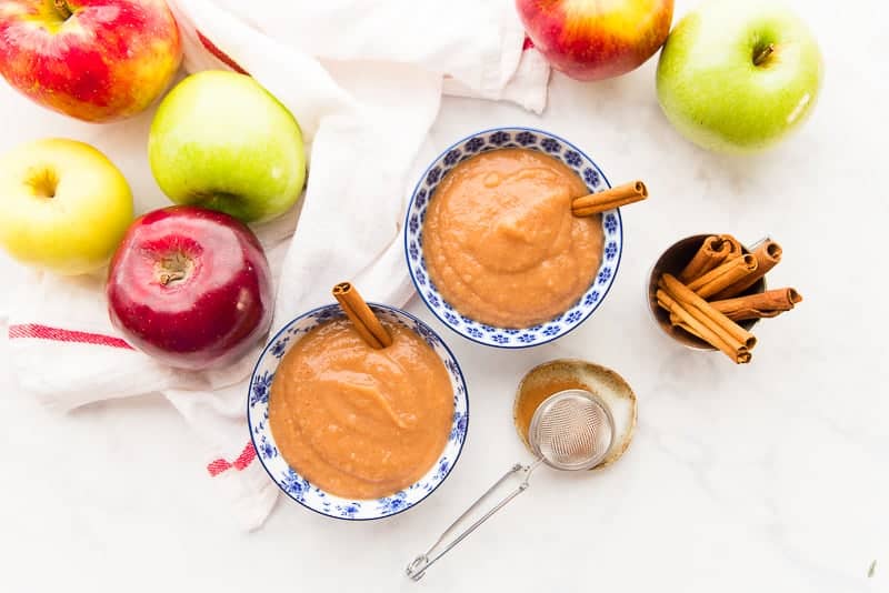 Horizontal image of two blue and white bowls of slow cooker cinnamon applesauce surrounded by apples