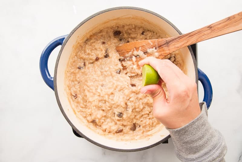 A hand squeezes half a lime over a pot of arroz con dulce.
