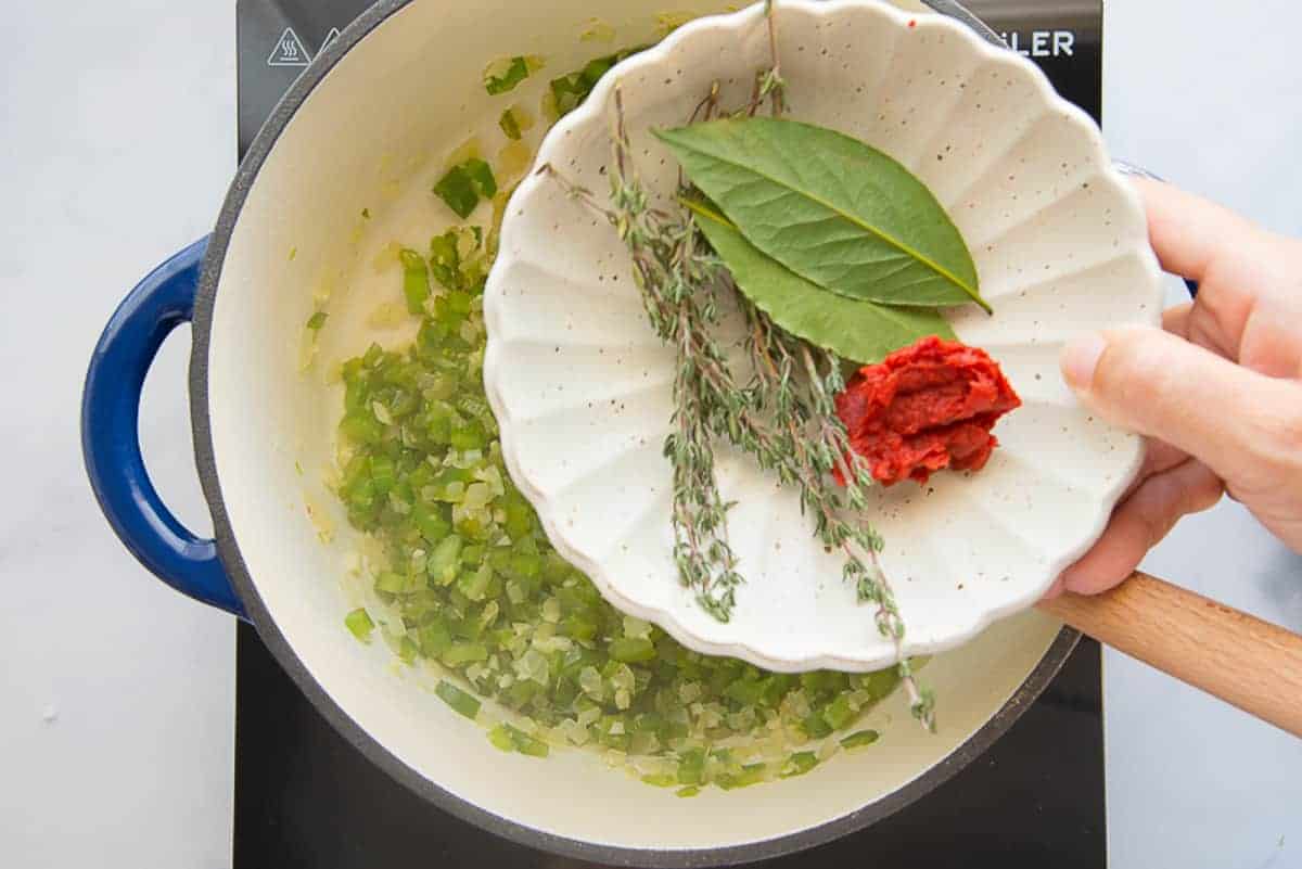 Bay leaves, thyme, and tomato paste are added to the veggies in the blue pot