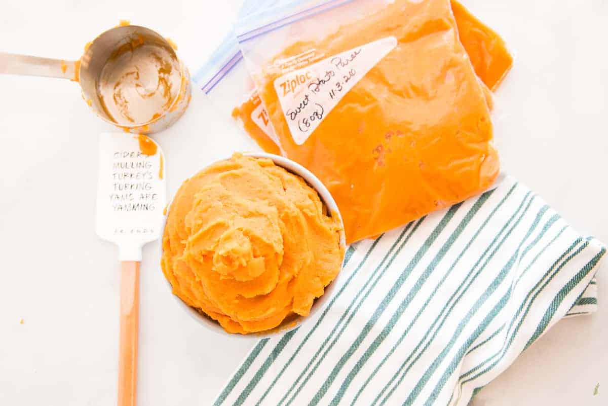 Sweet potato puree in a gray bowl next to a green and white striped kitchen towel bags filled with sweet potato puree are marked with a date