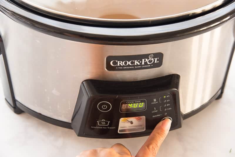Finger pushes buttons to is turn on a slow cooker.