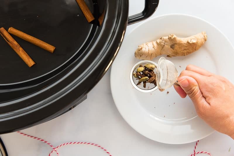 Whole spices are added to a tea strainer before being placed into a slow cooker.