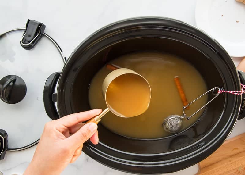 Apple cider is poured from the measuring cup into the slow cooker